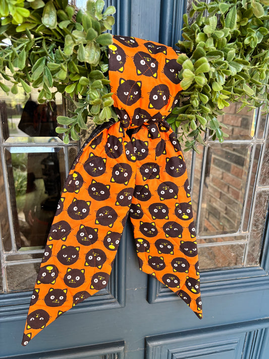 Orange whimsical wreath sash with black cats  tied on a wreath, against a blue door creates a statement entry way. 