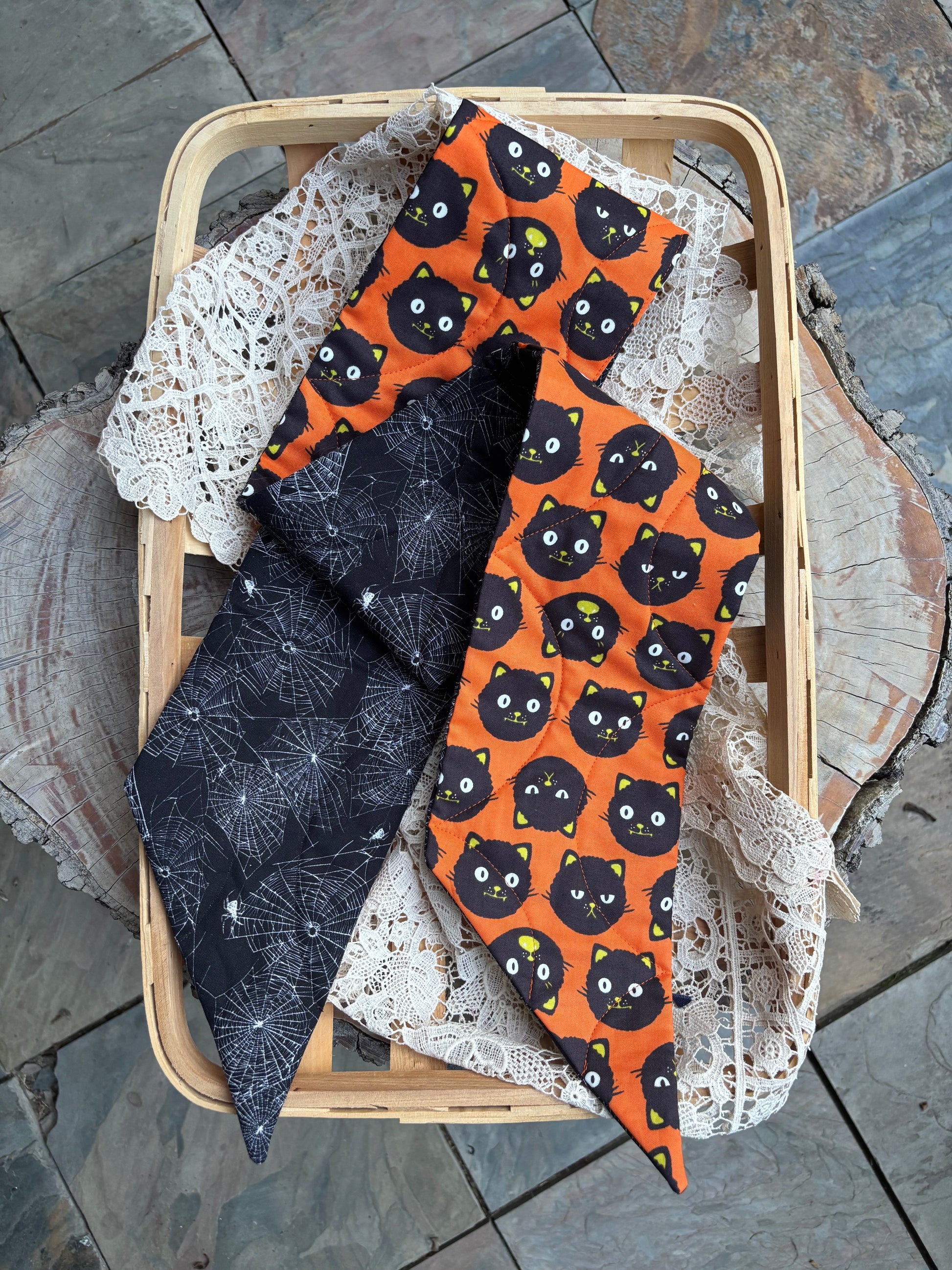 Reversible Halloween quilted wreath sash with black cats and spiderwebs displayed in an open basket with lace. 